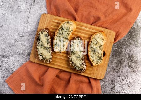 Gegrillte Sandwiches mit Knoblauch und geschmolzenem Käse mit Kräutern auf einem Holzbrett mit dunkelgrauem Hintergrund. Draufsicht, flach liegend Stockfoto