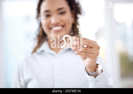 Hand, Hörgerät und Versicherung mit einer schwarzen Frau, die ein Abhörgerät in einer Klinik hält. Medizin, Technik und Audiologie bei einer Frau Stockfoto