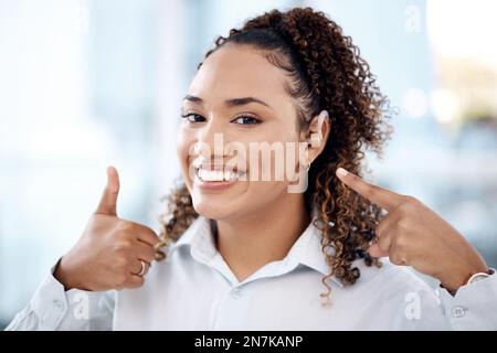 Daumen hoch, glücklich und Porträt einer Frau mit einem Hörgerät, das auf ihr Ohr im Büro zeigt. Glück, Erfolg und junge Berufstätige mit einer Stockfoto