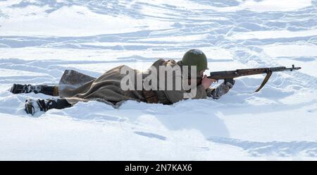 KRASNOE SELO, RUSSLAND - 05. FEBRUAR 2023: Der sowjetische Soldat liegt im Schnee und zielt mit einem SVT-40-Selbstladegewehr von Tokarev. Militärisch-historische Aufklärung Stockfoto