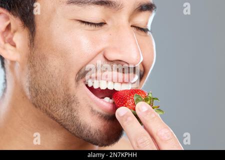Ein Biss der Güte. Ein Mann, der vor einem grauen Hintergrund eine Erdbeere beißt. Stockfoto