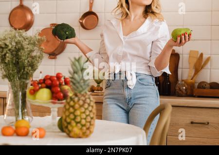 Eine Frau in der Küche hält Gemüse und Obst in der Hand. Gemüse und Obst liegen auf dem Tisch mit weichem Fokus. Kochen. Stockfoto