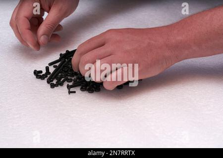 2 Hände suchen schwarze Schraube auf einem Bolzenhaufen. Verbindungselemente für Industrie und Handwerk. Stockfoto