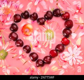 Herzförmiges süßes Kirschmuster und Blumen auf Rosenwasser, flach liegend Stockfoto