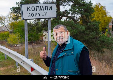Portrait eines positiven UkrinianSenioren, der auf der Autobahn Kharkiv-poltava steht, neues Schild, das das Dorf Kopyly, Ukraine, markiert Stockfoto