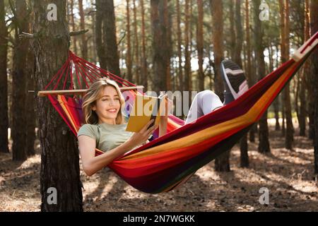 Frau mit Buch, die sich am Sommertag in der Hängematte im Freien entspannen kann Stockfoto