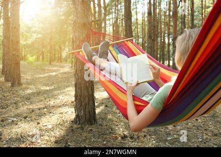 Frau mit Buch, die sich am Sommertag in der Hängematte im Freien entspannen kann Stockfoto