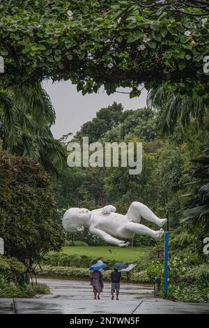 Regnerischer Tag in den Gärten an der Bucht, Singapur, mit zwei Personen, die zu Fuß unterwegs sind, und der Skulptur eines schlafenden Kindes, das in der Luft schwimmendes Baby namens Planet Stockfoto