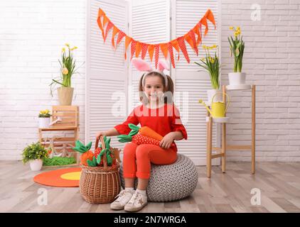 Ein bezauberndes kleines Mädchen mit Hasenohren und Spielzeugmöhren im Osterfoto-Bereich Stockfoto