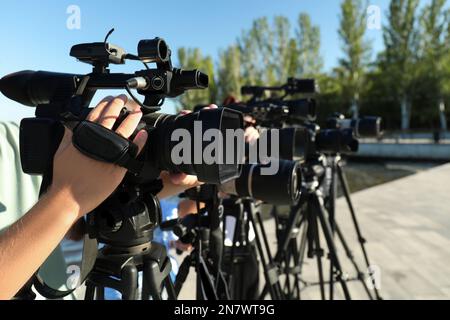 Mitarbeiter mit professionellen Videokameras, die an sonnigen Tagen im Freien arbeiten, Nahaufnahme Stockfoto