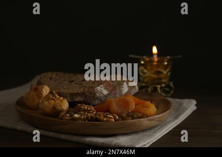 Brot, getrocknete Früchte, Walnüsse und brennende Kerze auf einem Holztisch. Tolle Fastenzeit Stockfoto