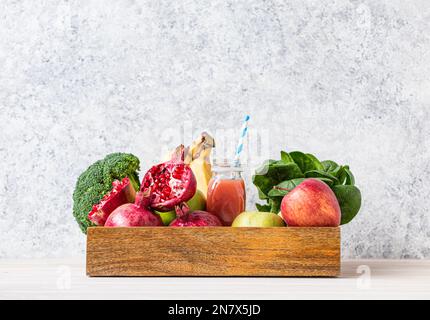 Obst, Gemüse, Gemüse in einer Holzschale und frischer Smoothie oder Saft in der Flasche mit Papierstroh auf dem Tisch nahe der weißen Wand, Entgiftung, Diät, sauberes Essen Stockfoto
