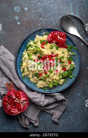 Farbenfroher Couscous- oder Bulgur-Salat mit Granatapfelsamen Tabbouleh in rustikal blauer Keramikschale, Blick von oben auf Betonhintergrund, traditionell Stockfoto
