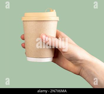 Pappbecher Kraft, Kaffeetasse zum Mitnehmen in der Hand auf grünem Hintergrund. Craft-Kaffee, heißes Getränk zum Mitnehmen. Stockfoto