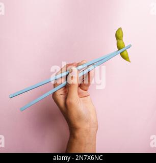 Handgehaltene Essstäbchen mit Edamamabohne Stockfoto