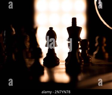Eine Nahaufnahme von König- und Königin-Schachfiguren auf einem Schachbrett im Schatten Stockfoto