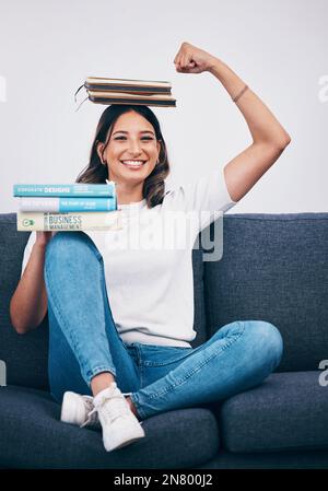 Porträt, Bildung und Erfolg mit einer Studentin, die ihren Bizeps beugt, während sie zu Hause auf dem Sofa sitzt. Universität, Bücher und Waage mit einem Stockfoto