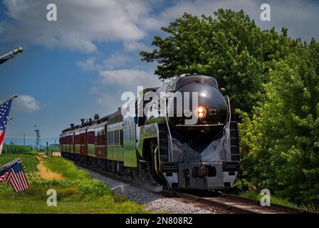 An einem sonnigen Sommertag fährt ein restaurierter Dampf-Passagierzug an, während American Flags auf einem Zaun im Zug durch Ackerland fahren Stockfoto