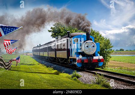 Strasburg, Pennsylvania. Juni 18 2021 - Blick auf Thomas, den Zug, der an einem sonnigen Tag an amerikanischen Flaggen vorbeifährt und dabei Passagierwagen zieht Stockfoto