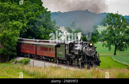 Ronks, Pennsylvania, 18. Juni 2021 - Blick auf einen restaurierten Dampfzug, der sich an einem Sommertag mit Rauch und Dampf aus dem Wald nähert Stockfoto