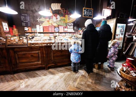 Ternopil, Ukraine - 10. Februar 2023: Mutter und drei Kinder kaufen am Winterabend Süßigkeiten in der Schokoladenwerkstatt. Stockfoto