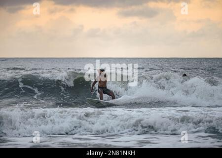 Eine Person, die bei Sonnenuntergang in Cenang Beach, Langkawi, Malaysia surft. Stockfoto