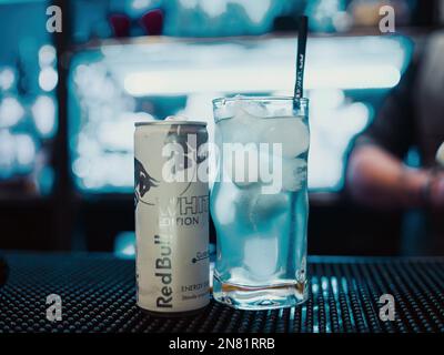 Eine redaktionelle Abbildung, die eine Dose RedBull White Edition auf einer Theke neben einem Glas mit Eis und einem Strohhalm zeigt. Die Schärfentiefe ist sehr nar Stockfoto