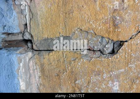 Die alten schäbigen Wände des alten Hauses, mit abblätternder Farbe gehauen, große und kleine Risse in der grauen Betonwand. Stockfoto