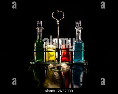Farbige Flaschen Olivenöl-Balsamico-Essig und Wein stehen auf dem Tisch und haben einen schwarzen Hintergrund. Stockfoto