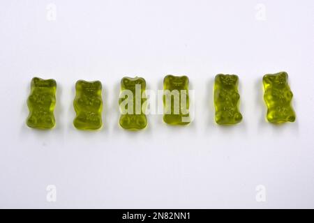 Leuchtend grünes Kauen, Süßigkeiten in Form und in Form von farbigen Bären liegen auf weißem Hintergrund. Stockfoto