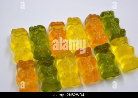 Leuchtende orangefarbene, grüne, gelbe Kaubonbons in Form und in Form von farbigen Bären liegen auf weißem Hintergrund. Stockfoto