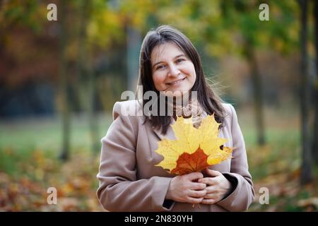 Lächelnde Frau mit Herbstapfelblättern im Freien. Selektiver Fokus. Stockfoto