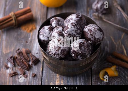 Weiche vegane, gedämpfte Schokoladen-Lebkuchen mit Puderzucker in einer alten Schüssel und Zutaten, Gewürzen, Schokolade, Orange auf einem Holztisch Stockfoto