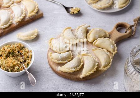 Hausgemachte rohe gefrorene vegane Knödel, Vareniki, Pierogi, Kreplach gefüllt mit veganem Linsenfleisch, Karotten, Zwiebeln, Kräutern und Gewürzen auf Holzbrett Stockfoto