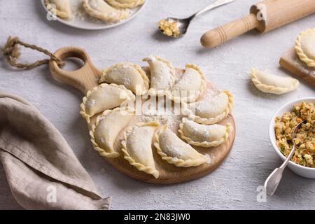 Hausgemachte rohe gefrorene vegane Knödel, Vareniki, Pierogi, Kreplach gefüllt mit veganem Linsenfleisch, Karotten, Zwiebeln, Kräutern und Gewürzen auf Holzbrett Stockfoto