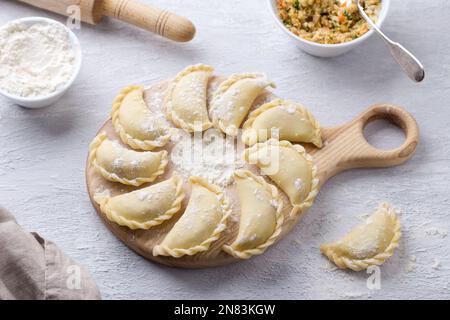 Hausgemachte rohe gefrorene vegane Knödel, Vareniki, Pierogi, Kreplach gefüllt mit veganem Linsenfleisch, Karotten, Zwiebeln, Kräutern und Gewürzen auf Holzbrett Stockfoto