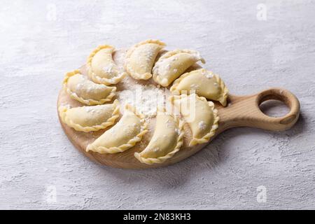 Hausgemachte rohe gefrorene vegane Knödel, Vareniki, Pierogi, Kreplach gefüllt mit veganem Linsenfleisch, Karotten, Zwiebeln, Kräutern und Gewürzen auf Holzbrett Stockfoto