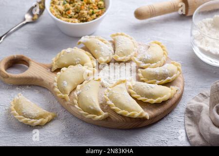 Hausgemachte rohe gefrorene vegane Knödel, Vareniki, Pierogi, Kreplach gefüllt mit veganem Linsenfleisch, Karotten, Zwiebeln, Kräutern und Gewürzen auf Holzbrett Stockfoto