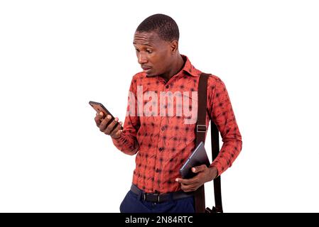 Porträt eines überraschten jungen Geschäftsmanns, der auf ein Mobiltelefon schaut und ein digitales Tablet in der Hand hält. Stockfoto