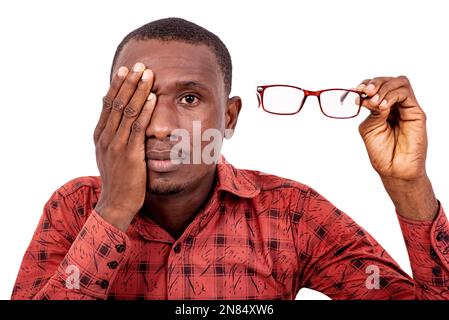 Ein gutaussehender Mann in einem karierten Hemd, der auf weißem Hintergrund steht, ein Auge mit der Hand bedeckt und eine Brille hält. Stockfoto