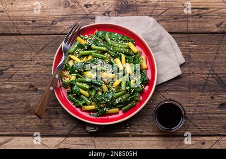 Grüne und gelbe Bohnen mit Spinat, Sesam und Sojasauce auf Holztisch, Draufsicht Stockfoto