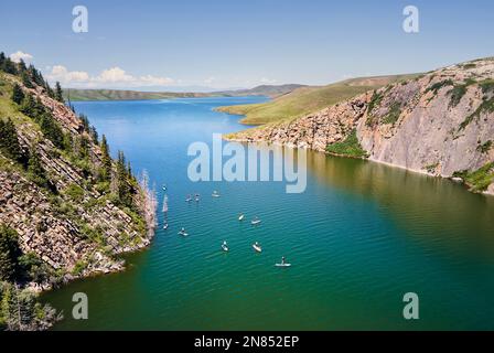 Top-down-Drohnenaufnahme von einer Gruppe von Menschen auf Stand-Up-Paddle-Boards SUP im Bergsee in der Nähe von Felsen mit Fichtenwald in Kasachstan Stockfoto