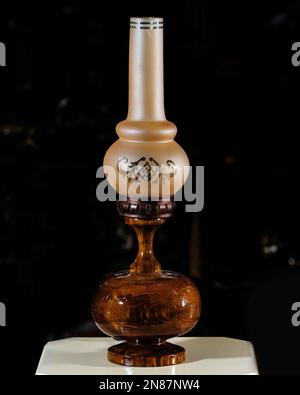 Eine alte, braune, hölzerne Nachtlampe auf einem weißen Tisch mit schwarzem Hintergrund. Stockfoto