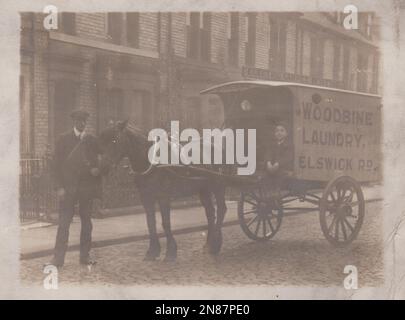 Lieferwagen und Pferd für die Woodbine Wäscherei, Elswick Road, Newcastle auf Tyne. Ein kleiner Junge sitzt und lächelt auf dem Wagen, während ein Mann mit einer flachen Mütze die Zügel des Pferdes hält. Ein Schild mit der Aufschrift „Elektrischer Teppichstaub“ ist auf einem Gebäude hinter dem Transport zu sehen