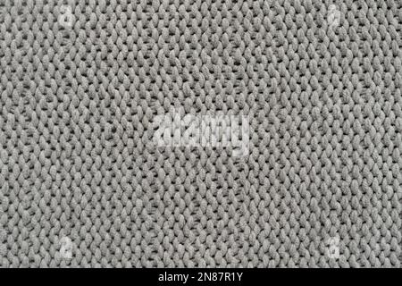 Gestrickter grauer Hintergrund. Nahaufnahme einer Strickdecke. Wellenförmig faltet Material. Strickpullover oder Schal in warmem Grau. Banner, Kopierbereich. Stockfoto