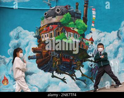 Kinder posieren für ein Foto vor einem Wandgemälde mit Howl's Moving Castle in Central vom Künstler Pei Chung aus Hongkong. 04FEB23 SCMP/Yik Yeung-man Stockfoto