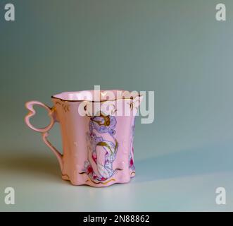 In der Tschechischen Republik wird ein rosafarbener Porzellanbecher in ungewöhnlicher Form hergestellt. Eine Tasse mit einem romantischen Muster auf weißem Hintergrund. Stockfoto