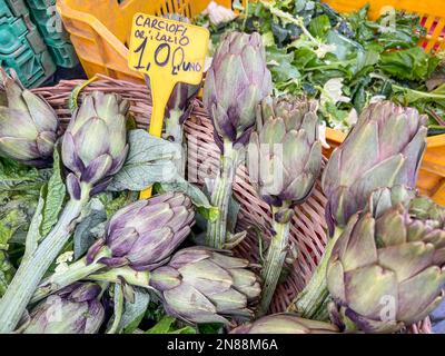 Supermarkt, italienisches Preisschild auf frischen Artischocken mit selektivem Fokus auf einem offenen Bauernmarkt in Italien. Frische und reife Artischocke auf Gemüsestan Stockfoto