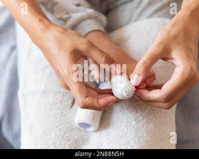 Mutter verbindet den großen Zeh ihres Kindes. Nahaufnahme des Kinderfußes mit Bandfinger. Erste Hilfe bei kleinen häuslichen Verletzungen. Stockfoto