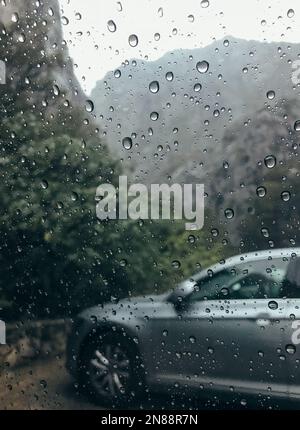 Regentropfen auf dem sauberen Autoglas-Bild mit silbernem Auto auf dem Hintergrund. Tief Herbst kalt regnerisch nebligen Tag Foto auf dem Berg Parkplatz. W Stockfoto